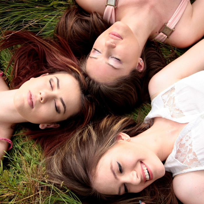 Three young women relax together on the grass, enjoying a sunny day and each other's company